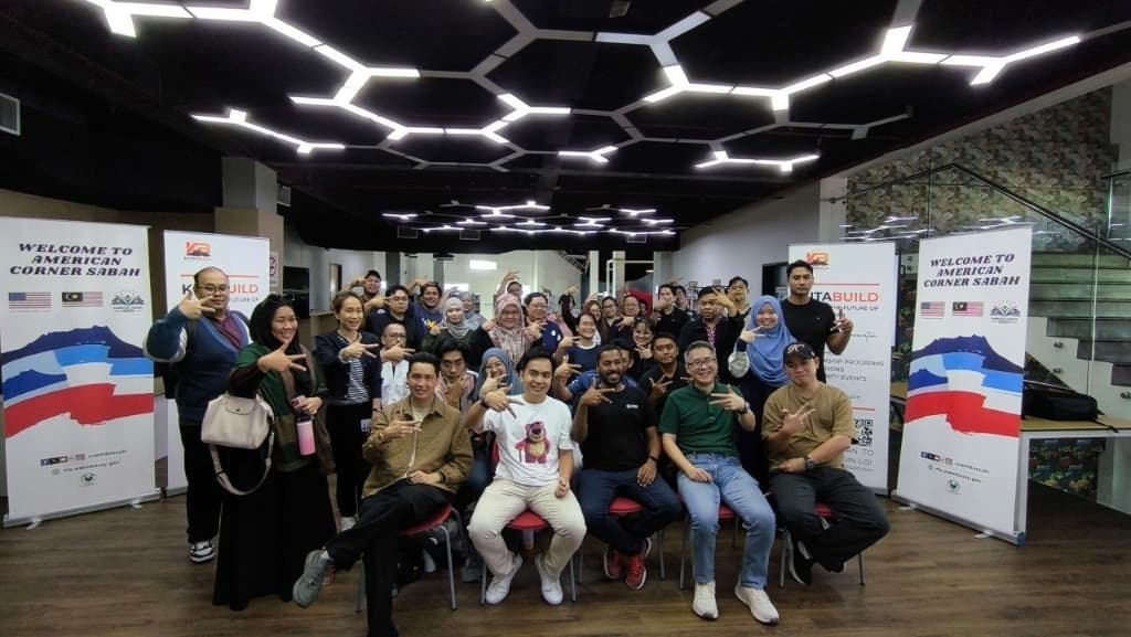 KitaBuild AI Sabah Community group photo with attendees making signature hand gesture at American Corner Sabah